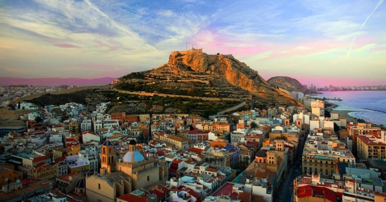 Vista panorámica de Alicante, con el Castillo de Santa Bárbara en lo alto, el puerto deportivo y el mar Mediterráneo al fondo, destacando el encanto de la ciudad costera